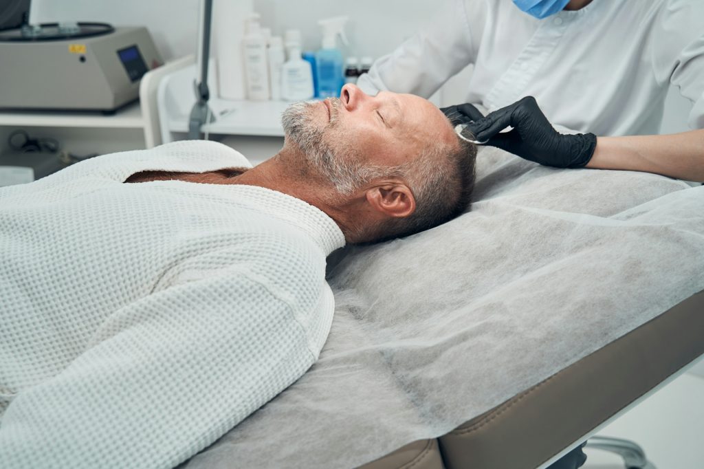 Man receiving hair loss treatment in cosmetology clinic-Guía completa del injerto capilar: Qué esperar antes, durante y después del tratamiento - Uve Medical, clinica de estetica facial y capilar